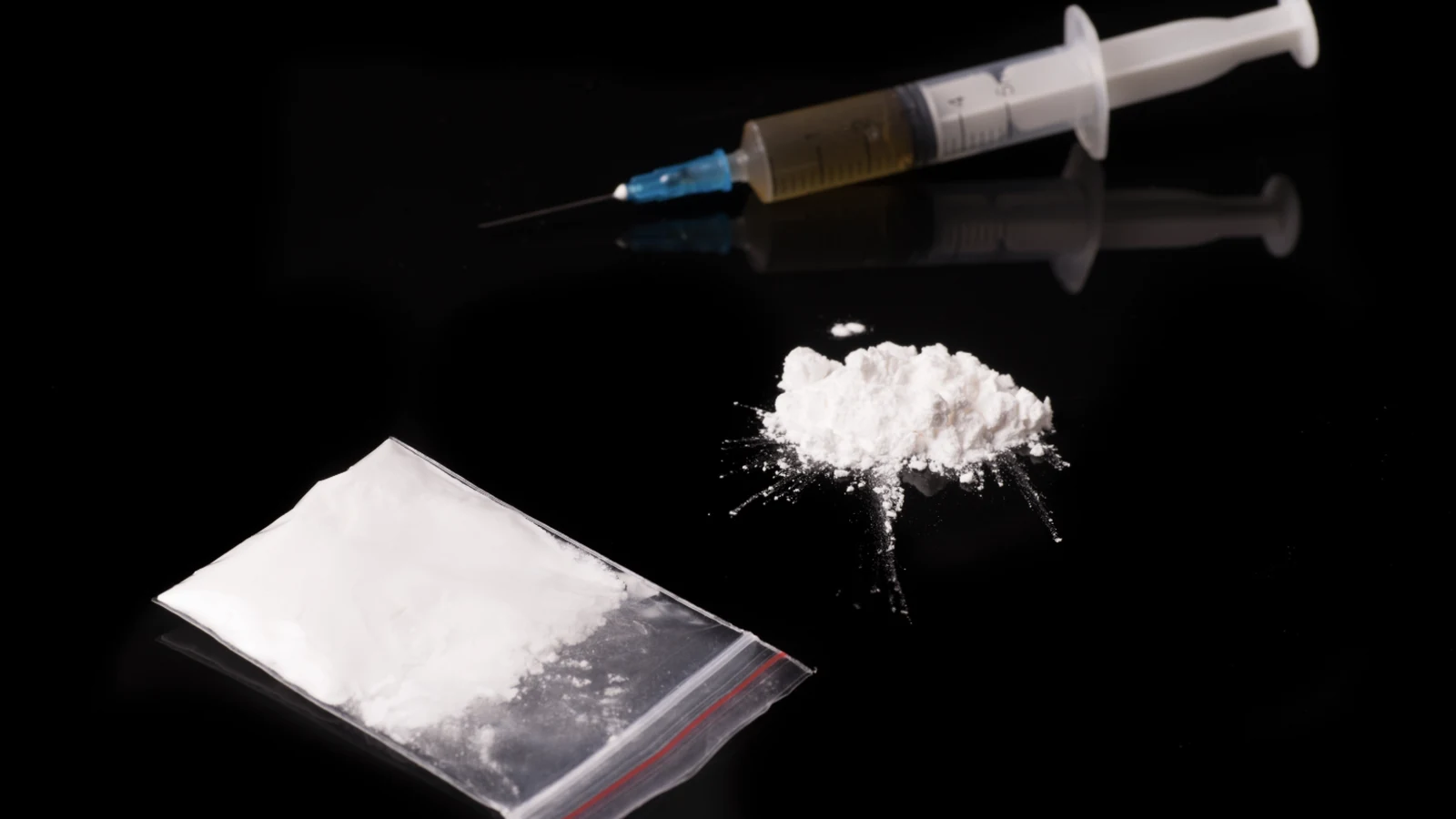 A public safety image showing illicit powder and a syringe on a dark surface.